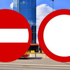 Dwa znaki drogowe: zakaz wjazdu (znak B-1) i okrągły znak zakazu. W tle nowoczesne budynki i tramwaj.