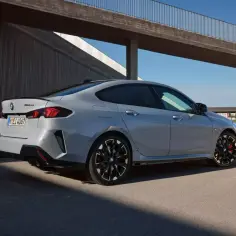 Szare BMW 2 Gran Coupé z czarnymi felgami i czerwonymi zaciskami hamulcowymi stoi na tle nowoczesnej architektury.
