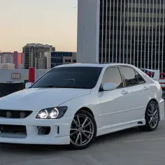 Biała Toyota Altezza z tuningiem stoi na parkingu, w tle widać wieżowiec Stratosphere i panoramę miasta o zachodzie słońca.