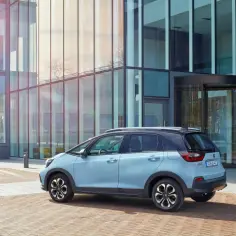 Jasnoniebieski Honda Jazz Crosstar stoi przed nowoczesnym budynkiem z przeszkloną fasadą.