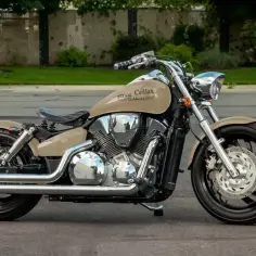 Beżowy motocykl Honda VTX 1300 z chromowanymi elementami i czarnym siedzeniem, zaparkowany na ulicy.