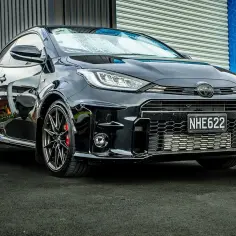 Czarny, sportowy toyota hatchback GR z agresywnym grillem i felgami stoi na ciemnym asfalcie.