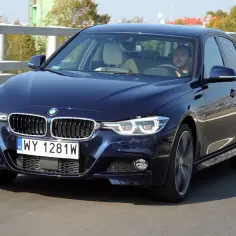 Ciemnoniebieskie BMW 320d xDrive jedzie po moście. Kierowca skupiony na drodze.