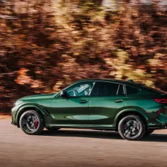 Zielone BMW X6M pędzi po drodze, rozmazane drzewa tworzą tło.