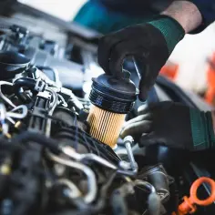 Mechanik w czarnych rękawiczkach wymienia filtr paliwa w silniku samochodu.