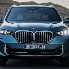 Nowy BMW X5 2024 w kolorze ciemnozielonym jedzie po pustynnej drodze.