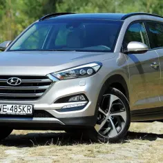 Srebrny Hyundai Tucson 2020 z czarnym dachem, zaparkowany na kamienistej drodze wśród zieleni.