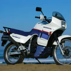 Biało-niebieski motocykl Honda Transalp 650 na plaży, gotowy na przygodę.