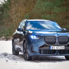 Nowe BMW X3 w zimowej scenerii lasu, gotowe na wyzwania śnieżnych dróg.