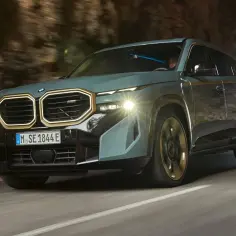 Nowoczesne BMW XM w kolorze szaro-zielonym przemierza krętą drogę, wyłaniając się z tunelu.