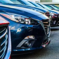 Błyszcząca, ciemnoniebieska osłona chłodnicy w samochodzie, obok innych aut na parkingu.