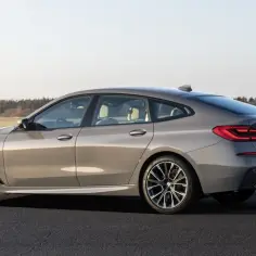 Eleganckie, szare BMW GT z jasnym wnętrzem stoi na asfalcie. W tle rozciąga się pole i las.