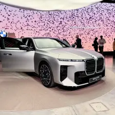 Eleganckie BMW M7 prezentuje się na wystawie, z otwartymi drzwiami, przyciągając uwagę gości.