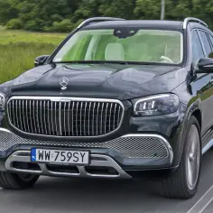 Elegancki Maybach GLS 600 w ciemnym kolorze pokonuje zakręt na drodze, otoczony zielenią.