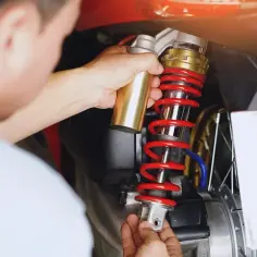 Mechanik dokonuje wymiany amortyzatorów w motocyklu, trzymając nowy element.