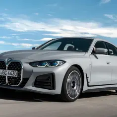 Szare BMW 4 Gran Coupé pędzi po drodze, otoczone zielenią i błękitnym niebem.
