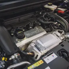 Silnik 1.6 PureTech z napisem "PEUGEOT SPORT" na metalowej osłonie. Widoczne przewody, turbosprężarka i elementy układu dolotowego.