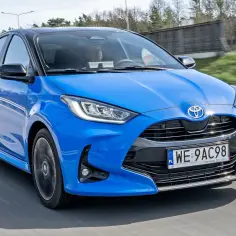 Niebieska Toyota Yaris 1. z czarnym dachem pędzi po drodze, kierowca skupiony na trasie.