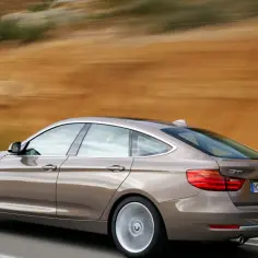 Brązowe BMW 3GT pędzi po krętej drodze, za nim rozmyty krajobraz.