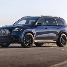 Lśniący, granatowy Mercedes GLS 580 z czarnymi felgami stoi na asfalcie przy plaży.