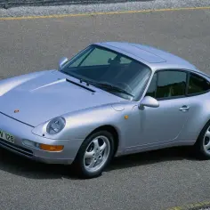 Srebrne Porsche 993 na drodze. Klasyczny design, okrągłe reflektory i charakterystyczna linia nadwozia.