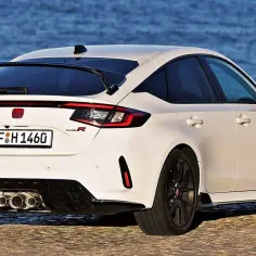 Biały Honda Civic Type R z dużym tylnym spojlerem i potrójnym wydechem, zaparkowany nad wodą.