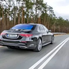 Czarny Mercedes S400d 4MATIC jedzie po drodze wśród drzew.