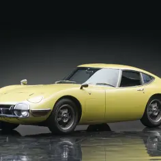 Żółta Toyota 2000GT z lat 60. na błyszczącej podłodze.