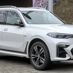 Białe BMW x7 z przyciemnianymi szybami i chromowanymi felgami stoi na brukowanym podjeździe.