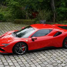 Czerwone Ferrari SF90 Stradale lśni na brukowanym podjeździe, otoczone zielenią.