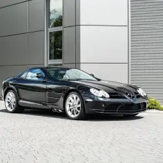 Czarny Mercedes McLaren SLR z połyskującymi felgami stoi przed nowoczesnym budynkiem.