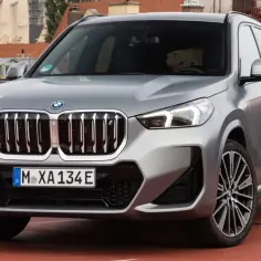 Srebrny BMW X1 2025 z charakterystycznym grillem i nowoczesnymi światłami, zaparkowany na tle miejskiej panoramy.