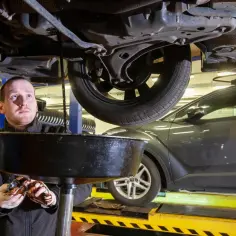 Mechanik spuszcza zużyty olej z samochodu. Zastanawiasz się nad wymiana oleju koszt? To kluczowy element dbania o silnik.