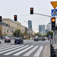 Skrzyżowanie z sygnalizacją świetlną, gdzie po jakim czasie przychodzi mandat za przejazd na czerwonym świetle? Widać samochody, tramwaj i billboard.