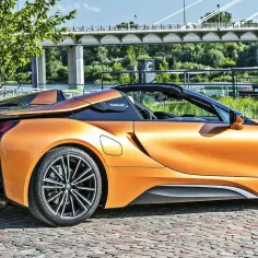 Pomarańczowy BMW i8 Roadster na bruku. Futurystyczny design, sportowe felgi. Sprawdź aktualną bmw i8 cena.