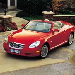 Czerwony Lexus SC430 z otwartym dachem, zaparkowany na podjeździe przed luksusowym domem.