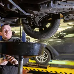 Mechanik spuszcza zużyty olej z samochodu. Zastanawiasz się nad wymiana oleju koszt? To kluczowy element dbania o silnik.