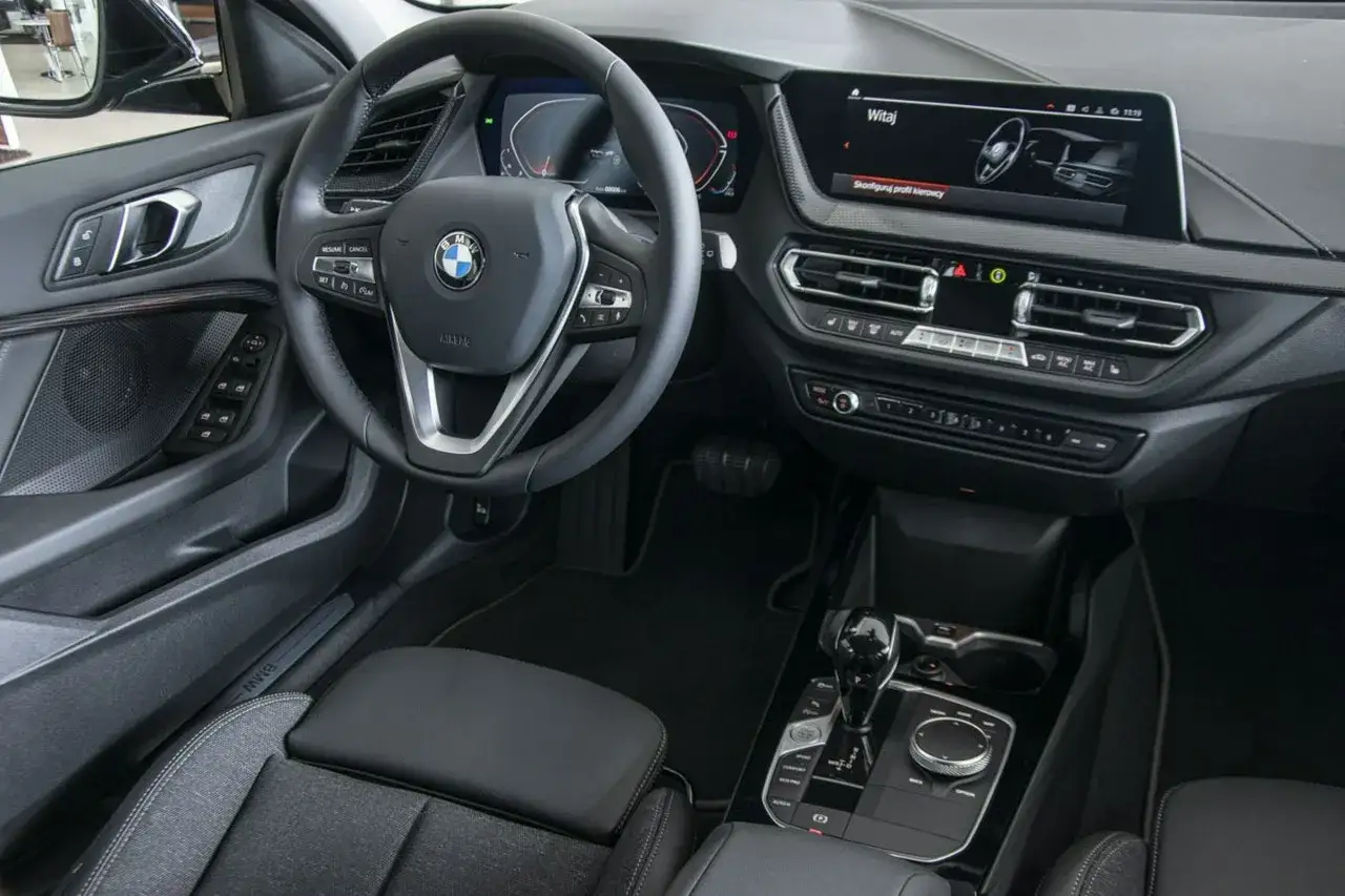 Wnętrze BMW 118i: kierownica, cyfrowe zegary, ekran multimediów i automatyczna skrzynia biegów.