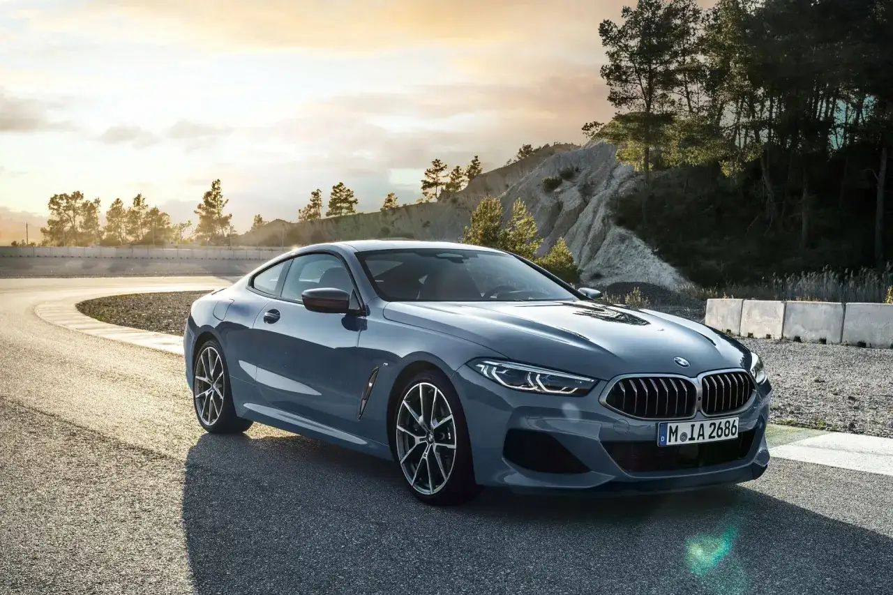 Szary BMW 840d na zakręcie toru wyścigowego, z drzewami i wzgórzami w tle.