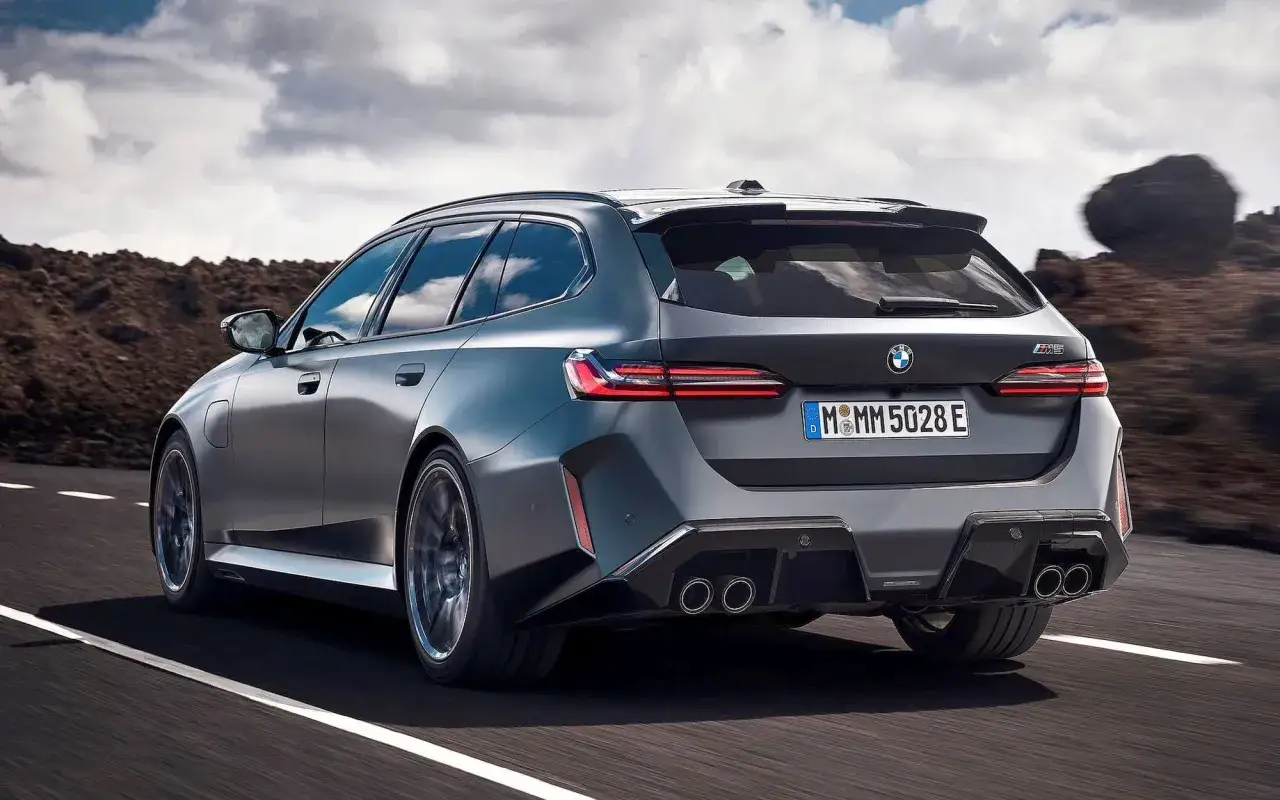 Szare BMW M5 Touring pędzi po drodze, ukazując swoje sportowe linie i cztery końcówki wydechu.