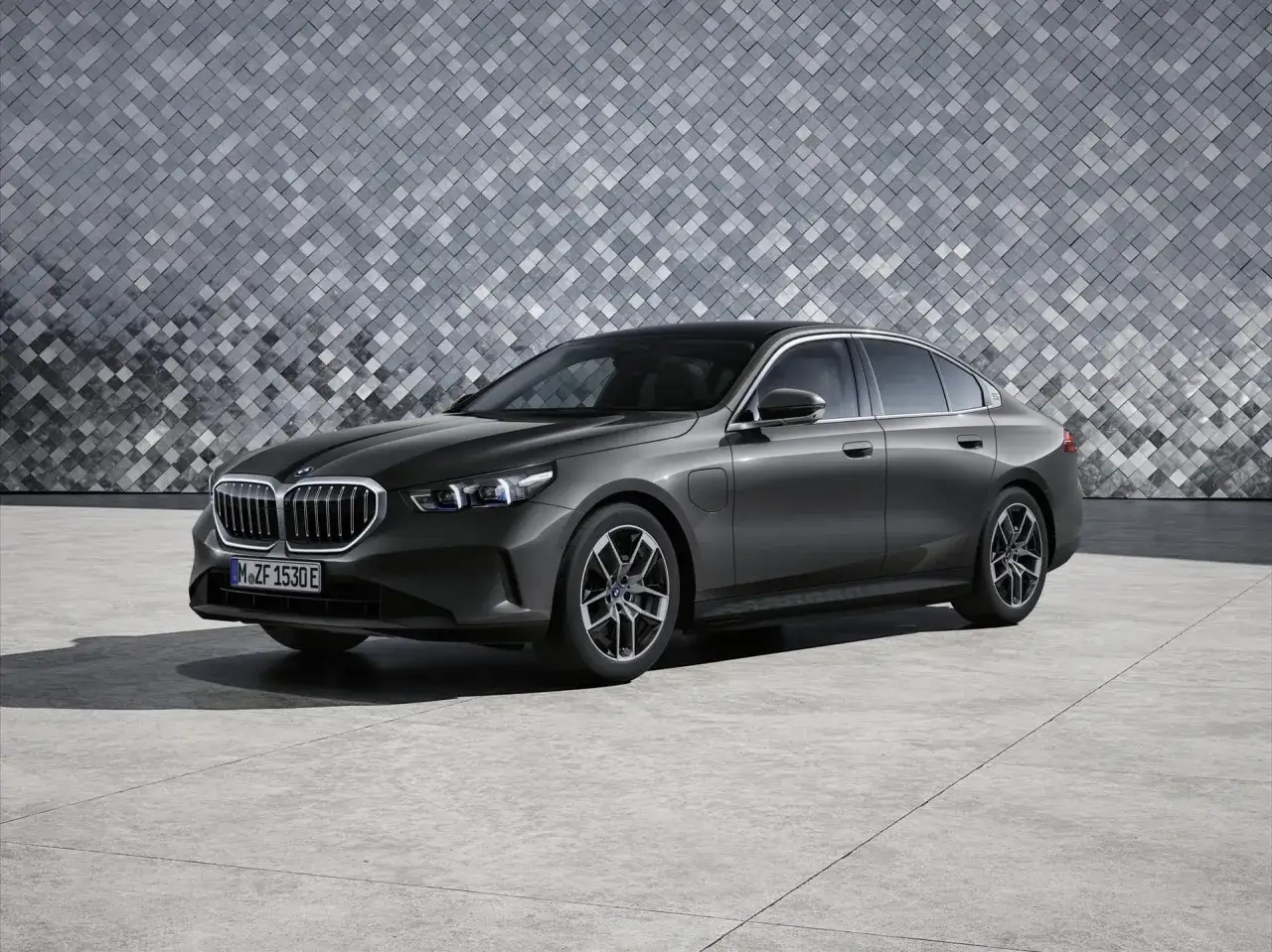 Eleganckie BMW 530e w kolorze grafitowym stoi na tle nowoczesnej, geometrycznej ściany.