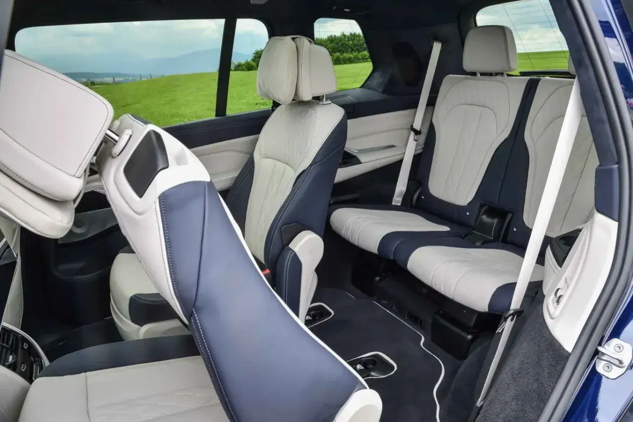 Wnętrze luksusowego BMW x7 z dwukolorową tapicerką. Widok na wygodne fotele i krajobraz za oknem.