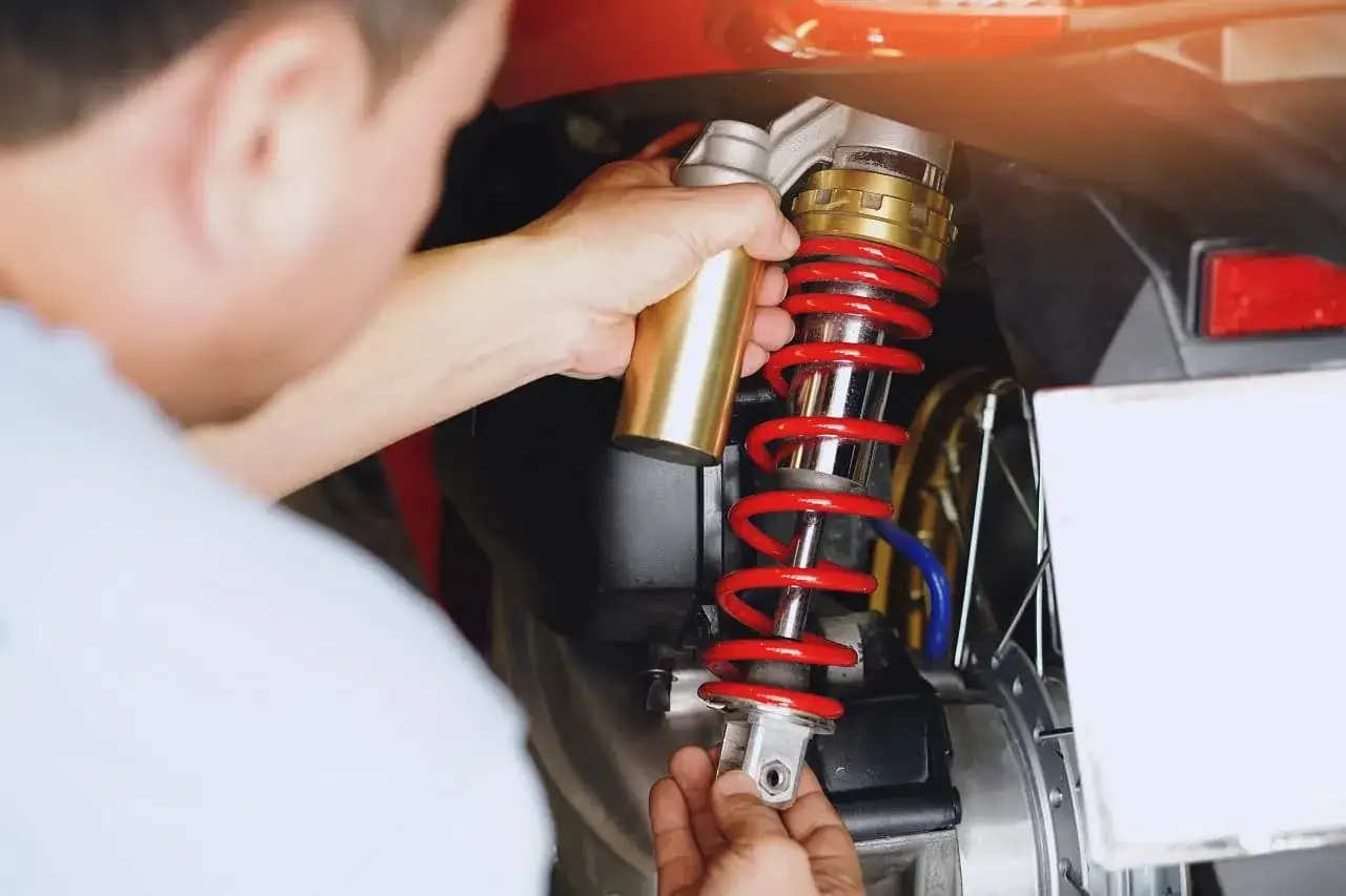 Mechanik dokonuje wymiany amortyzatorów w skuterze, trzymając nowy element.