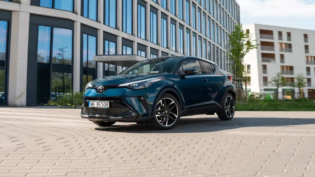 Elegancka Toyota C-HR, jeden z popularnych modeli hybrydowych, parkuje przed nowoczesnym budynkiem.