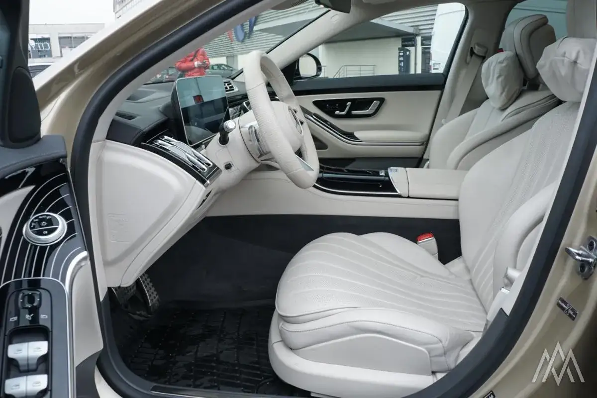 Wnętrze luksusowego Mercedesa S400d z jasną, skórzaną tapicerką, nowoczesnym kokpitem i dużym ekranem multimedialnym.