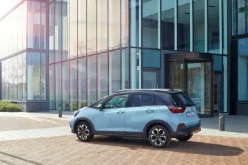 Jasnoniebieski Honda Jazz Crosstar stoi przed nowoczesnym budynkiem z przeszkloną fasadą.