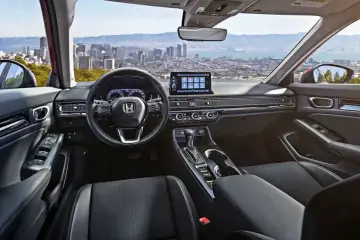 Wnętrze nowego Honda Civic 11 z widokiem na miasto. Skórzana tapicerka, nowoczesny ekran i kierownica.