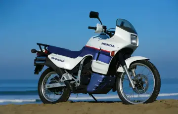 Biało-niebieski motocykl Honda Transalp 650 na plaży, gotowy na przygodę.