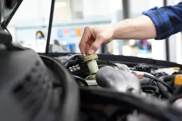 Ręka mechanika dokręca korek zbiorniczka płynu hamulcowego. Czas na badanie techniczne po terminie, by uniknąć problemów.