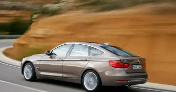 Brązowe BMW 3GT pędzi po krętej drodze, za nim rozmyty krajobraz.